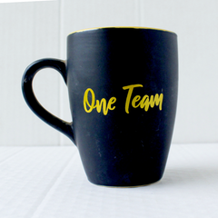 A black ceramic mug with 'One Team' text in yellow.
