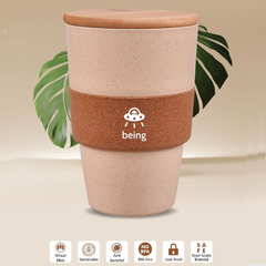 A beige and brown eco-friendly cork sipper mug with a logo on the band, displayed with leaves in the background.