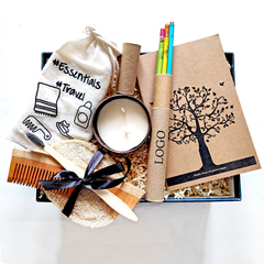 A gift basket containing a candle, wooden pencils, a notebook, a bamboo toothbrush, a cotton drawstring bag, and a pumice stone.