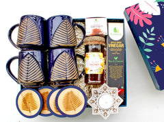 A luxurious Diwali gift hamper containing artisanal ceramic coffee mugs, coasters, natural honey, saffron, apple cider, and a wooden carved tea light holder, all presented in a decorative box.