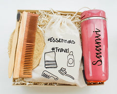 A gift box set including a pink personalized flask, a neem wood comb, a bamboo toothbrush, a sustainable loofah, and an eco-friendly bag.