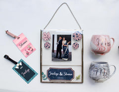 A collection of personalized anniversary keepsakes including a gold-rimmed double glass frame, a Mr. and Mrs. bag, cups and luggage tags