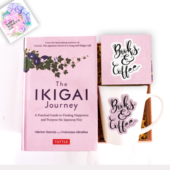 The image features a set of books and coffee items, including a pink mug with 'Books & Coffee' text, a white coaster with a floral design, and a pink box with 'The Ikigai Journey' book. There's also a decorative flower in the background.