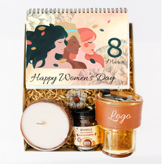 A gift set containing a Women's Day calendar, a glass tumbler with vegan leather accents and a straw, a coconut shell scented candle, and a customizable jar of gourmet coffee. The calendar features diverse women and has 'Happy Women's Day' text.