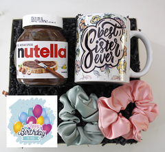 A birthday box containing a mug with 'Nutella' text and a graphic design, a jar of Nutella, a balloon, and a bow with an 'Happy Birthday' message.