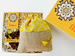 A designer-branded gift box containing a pouch of mixed cookies and a pack of organic scented potpourri, wrapped in yellow and checkered paper.