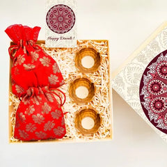 A gift set containing three gold metal tea light holders and two red fabric pouches with a printed design, presented in a white box with a decorative rim.