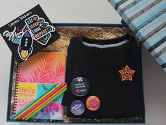 A corporate gift set including a black round neck t-shirt with a logo, colorful button badges, a spiral hardbound diary, eco-friendly paper pencils, laptop stickers, a message card, all packaged in a custom keepsake box.