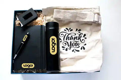 A set of corporate gifts including a black executive diary, a black executive stylus pen, a metal mobile phone stand, a beige cotton tote bag with text 'Thank You' printed on it, and a temperature display flask. 